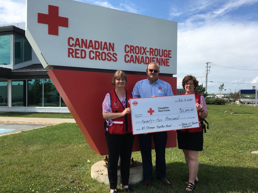 three union members holding a cheque standing in front of the Canadian Red Cross sign